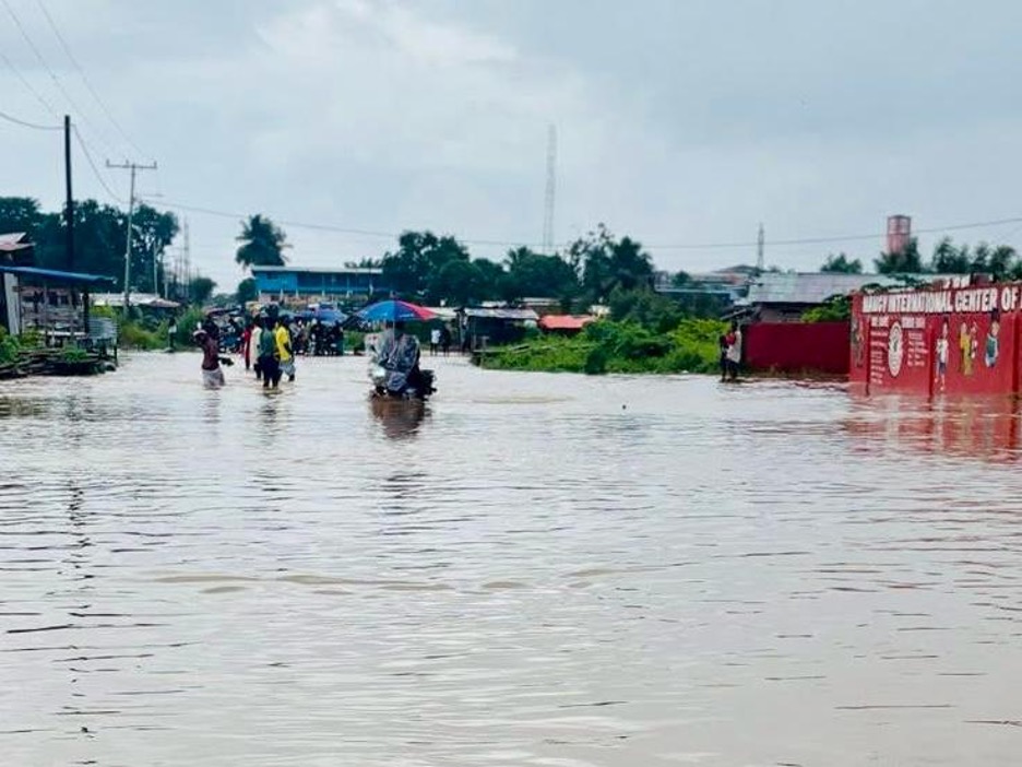Residents and motorcyclists navigate floodwaters on a community road in Peace Island, Jacob Town, near New Hope Junction, after heavy rainfall.